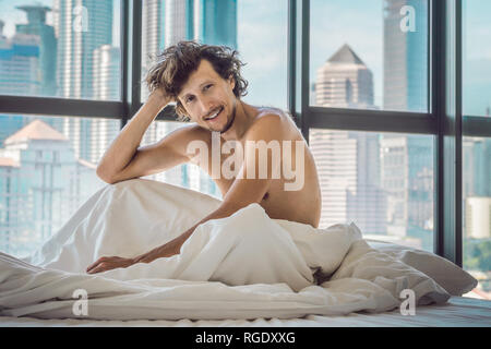 L uomo si sveglia al mattino in un appartamento nella zona del centro cittadino con una vista dei grattacieli. La vita in il rumore della città grande concetto. Non basta Foto Stock