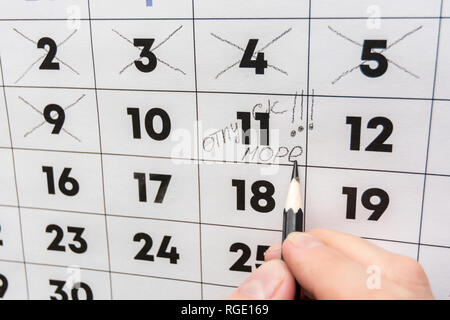 La mano con una matita scrive le parole vacanza e mare su un calendario da parete Foto Stock