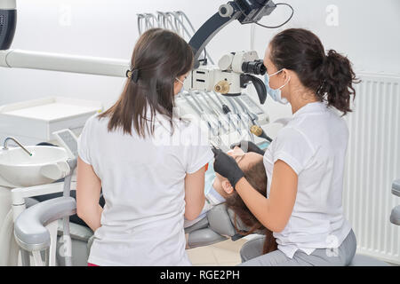 Vista dal retro della femmina di dentisti di lavoro e di controllare i denti del paziente di sesso femminile in studio dentistico. Giovane donna visita della clinica e preoccuparsi di denti. Concetto di odontoiatria e Stomatologia. Foto Stock