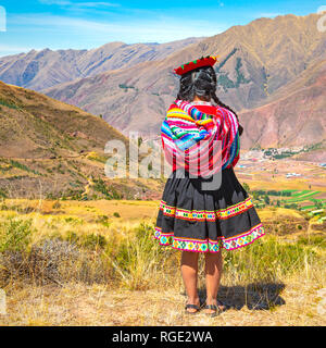 Formato quadrato di un indigeno Quechua lady in tradizionale stile di capelli, abito e hat guardando oltre la catena delle Ande in rovina Inca di Tipon, Perù. Foto Stock