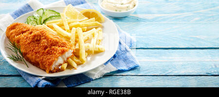 Impanati fritti filetto di merluzzo bianco servito con patate fritte e un'insalata di cetrioli su rustiche in legno blu nel panorama formato banner con spazio di copia Foto Stock