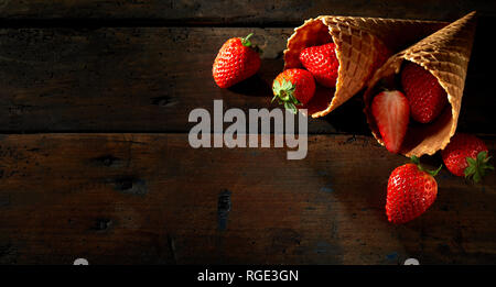 Cornette riempito di ripe rosso Fragole riversandosi su di un legno rustico superficie con spazio copia in formato grandangolare Foto Stock