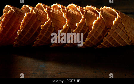 Vuoti accatastati o coni gelato coni di cialda sul tenebroso scuro legno rustico con evidenza per la tessitura e spazio di copia Foto Stock