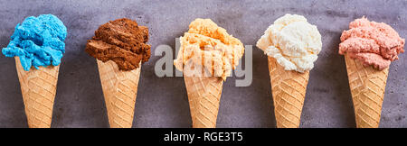 Panorama banner con un assortimento di diversi gusti di artisanal gelato servito in coni di zucchero in una fila su un sfondo di ardesia Foto Stock