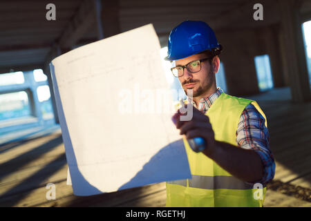 Voce maschile giovane architetto con blueprint utilizzando un walkie-talkie Foto Stock