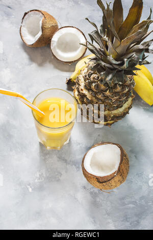 Ananas, banana e cocktail di noce di cocco o di succhi di frutta in vetro su uno sfondo di calcestruzzo Foto Stock