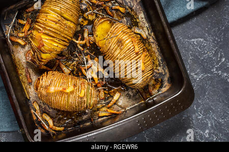 Arrosto di patate hasselback su ghisa pan. Sfondo scuro, vista dall'alto Foto Stock