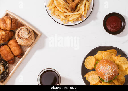 Pane appena sfornato, panini, grandi hamburger, fritto croccante di pollo e patatine fritte sul tavolo bianco - cibo malsano concetto Foto Stock