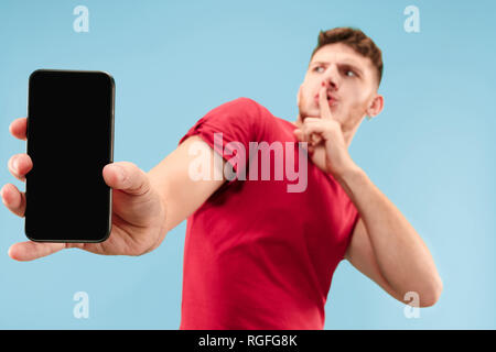 Ho paura. Spavento. Ritratto della paura l'uomo. Business man standing isolato sul trendy blue studio lo sfondo con il telefono cellulare. Le emozioni umane, espressione facciale concept Foto Stock