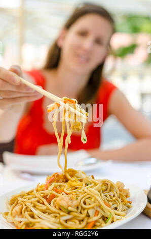 Giovane donna di mangiare cinese noodles fritti con gamberi e verdure. Foto Stock