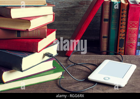 Ebook e di vecchi libri su un tavolo di legno. compressa scarica informazioni da molti libri. nuovo concetto tecnologico. tonificante vintage Foto Stock