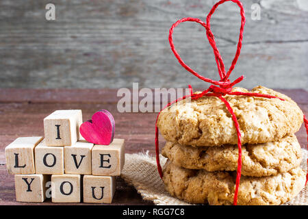 Ti amo iscrizione e fatti in casa i cookies di avena legato con cuore rosso a forma di nastro su un tavolo di legno. Il giorno di san valentino concetto Foto Stock