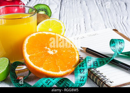 Il concetto di fitness con frutta e succo di frutta fresco. La motivazione di fitness con il centimetro e notebook bianco su sfondo di legno. close up Foto Stock