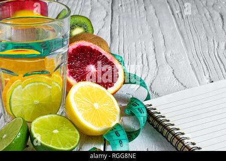 Il concetto di fitness con succhi di frutta e acqua detox. La motivazione di fitness con il centimetro e notebook bianco su sfondo di legno. close up Foto Stock