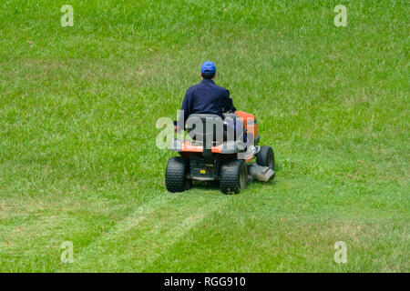 Angolo di alta vista posteriore di una persona Falciare il prato e il taglio dell'erba con un grande motorizzato tosaerba Foto Stock