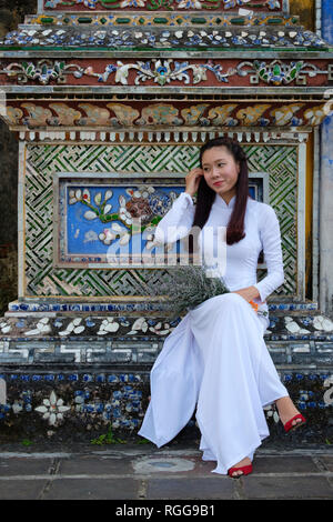 Ritratto di una giovane donna che indossa al tradizionale vietnamita indumento nazionale Áo dài mentre la visita della cittadella imperiale di Hue, Vietnam Asia Foto Stock