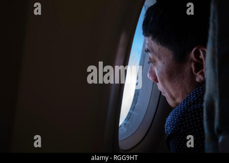 Uomo che guarda fuori dalla finestra di un aereo in volo Foto Stock