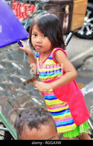 Manila, Philippines-October 24, 2016: Filippino ragazza giovane si prende cura del suo fratello più piccolo durante l'attesa per i loro genitori a comprare alcuni alimenti a stree Foto Stock