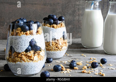 Mirtillo parfait di yogurt con granola e semi di Chia e bottiglie di latte per una sana prima colazione a tavola in legno rustico Foto Stock