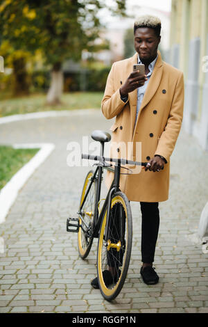 Ritratto di bel giovane utilizzando il telefono cellulare e il pignone fisso della bicicletta in strada. Foto Stock