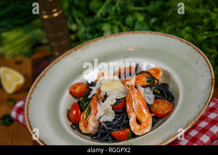 Nero pasta italiana con gamberetti, le verdure e le erbe su uno sfondo nero. Vista dall'alto. Foto Stock