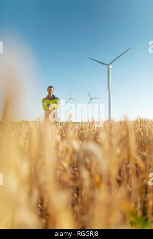 Ritratto di ingegnere sorridente in piedi in un campo di una fattoria eolica Foto Stock