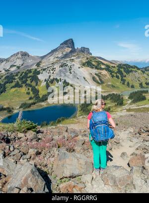 Escursionista sul sentiero escursionistico Panorama Ridge, piccoli laghi di fronte montagne, montagna vulcanica nero brosmio, Garibaldi Provincial Park Foto Stock