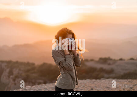 Spagna, Barcellona, parco naturale di Sant Llorenç, donna di scattare una foto con la fotocamera vintage al tramonto Foto Stock