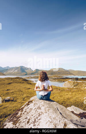 Norvegia Lofoten, vista posteriore della giovane donna seduta su una roccia facendo esercizi yoga Foto Stock