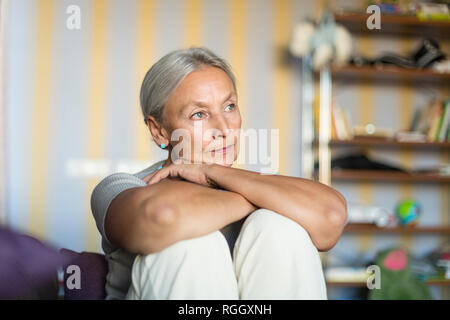 Ritratto di pensieroso senior donna seduta sul divano di casa Foto Stock