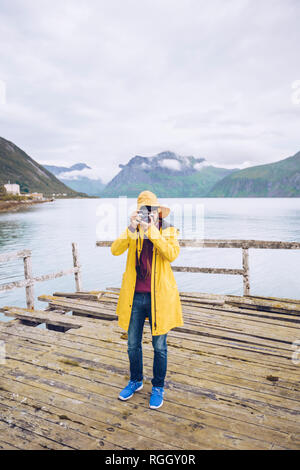 Norvegia, Senja, uomo in piedi su un molo sgangherato presso la costa di scattare una foto Foto Stock