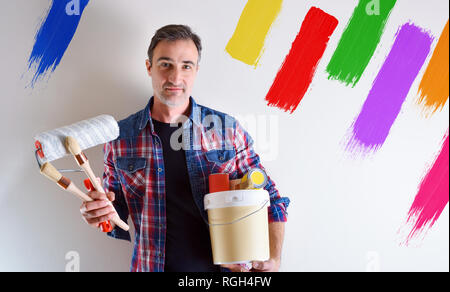 Uomo con materiale di vernice e gli utensili a mano e dei campioni di colore sulla parete. Vista frontale. Composizione orizzontale. Foto Stock