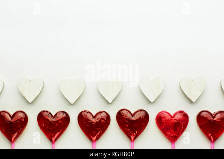 Modello di San Valentino con due righe di cuori - rosso lecca-lecca cuore bianco e cuori di legno Foto Stock
