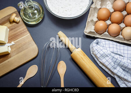 Utensili da cucina e gli ingredienti per la cottura di torte. Uova, farina e olio su sfondo scuro. Concetto di cottura, vista dall'alto angolo. Foto Stock
