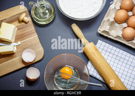 Utensili da cucina e gli ingredienti per la cottura di torte. Uova, farina, burro e olio su sfondo scuro. Concetto di cottura, vista dall'alto angolo. Foto Stock