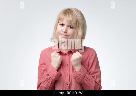 Timida donna con capelli biondi e prendere sul serio mantenendo i pugni rinserrata di fronte a lei per difendere se stessa Foto Stock