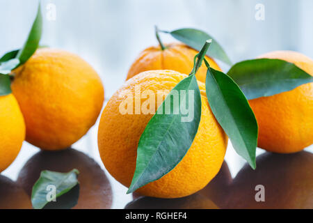 Un mucchio di freschi arance mature con foglie dal giardino su un tavolo di vetro, close-up studio shot Foto Stock
