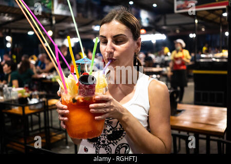 La ragazza beve un cocktail di grande da una cannuccia in un night club, un caffè notturno Foto Stock
