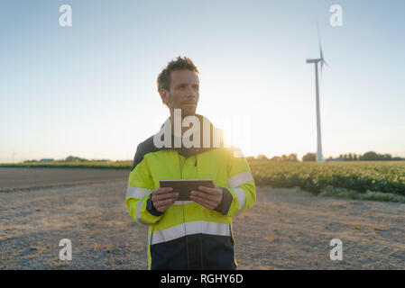 Ingegnere in piedi nel paesaggio rurale in una turbina eolica holding tablet Foto Stock