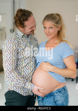 Uomo di toccare la pancia di sorridente donna in stato di gravidanza Foto Stock