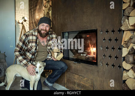 Ritratto di uomo sorridente con il suo cane di fronte al caminetto a casa Foto Stock