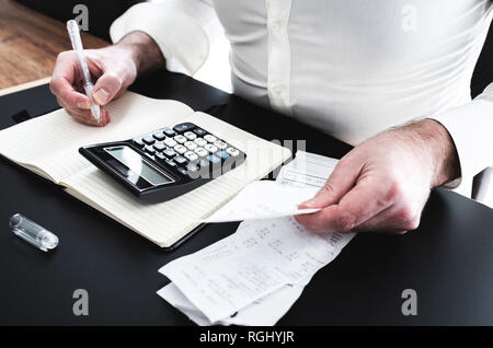 Uomo alla scrivania con la calcolatrice, le fatture di vendita o scivola e notpad Foto Stock