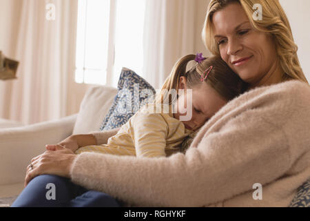 Vista laterale della madre amorevole abbracciando la sua accigliata figlia in armi a casa Foto Stock