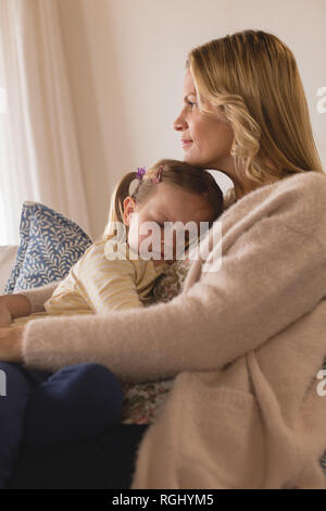 Vista laterale della madre sorridente abbracciando la sua figlia del sonno in armi a casa Foto Stock