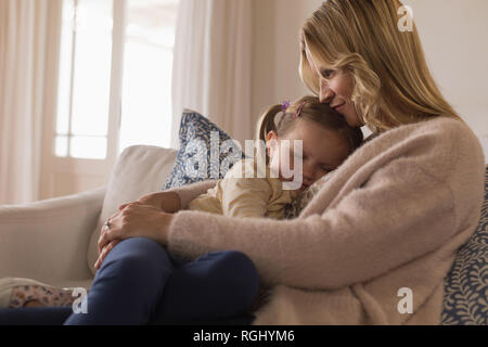 Vista laterale della madre amorevole abbracciando la sua figlia del sonno in armi a casa Foto Stock