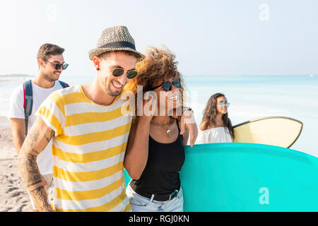 Gruppo di amici di camminare sulla spiaggia, portando le tavole da surf Foto Stock