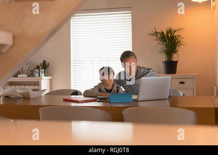 Vista frontale del padre amorevole aiutando il suo figlio con il suo dovere mentre utilizzando portatile a casa Foto Stock