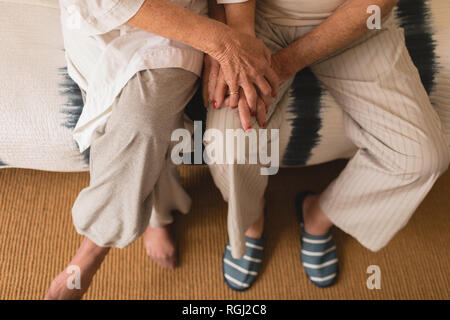 Sezione bassa della coppia senior tenendo le mani in camera da letto a casa Foto Stock