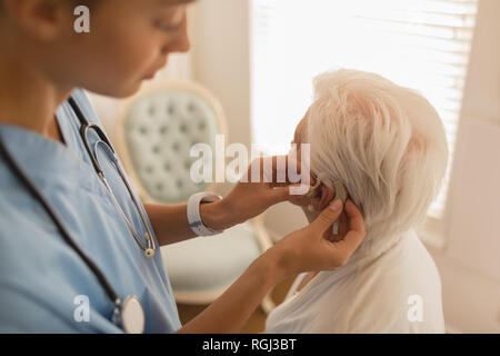 Medico femmina inserimento di protesi on senior womans orecchio a casa Foto Stock