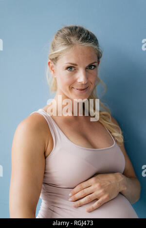 Ritratto di sorridere donna incinta in piedi alla parete blu Foto Stock